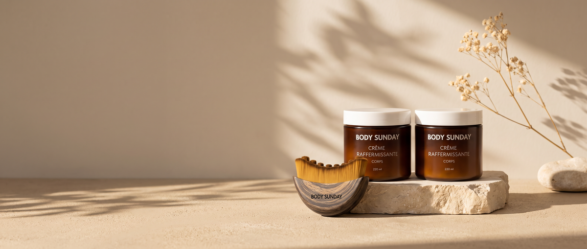 Duo Body Sunday : deux pots de crème raffermissante corps et brosse de massage posés sur une pierre claire, fond beige